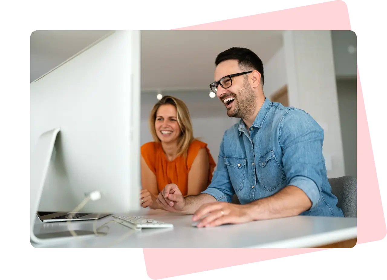 A man and a woman laughing while looking at a computer screen.