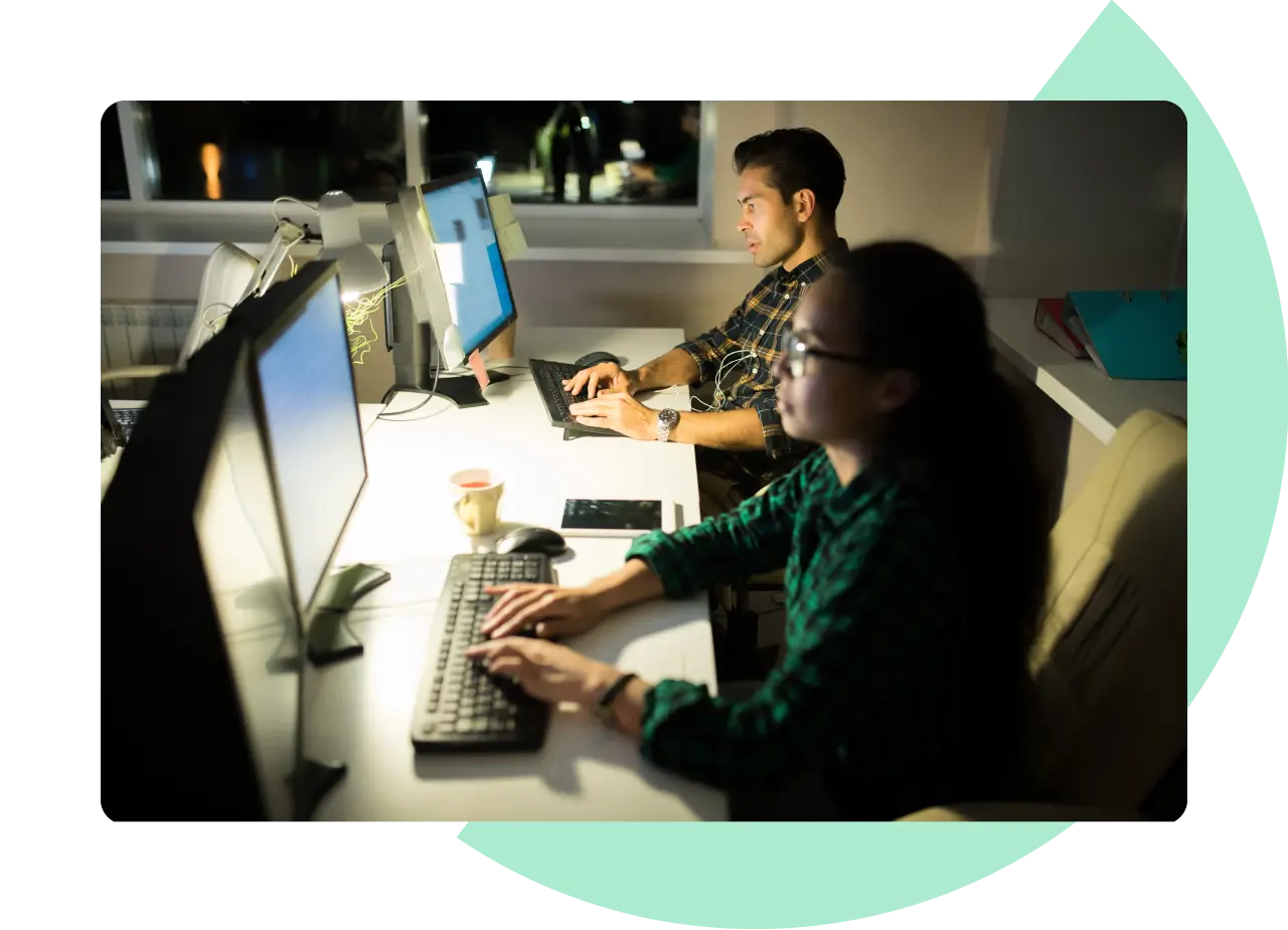 A femal and male software developer working on their computers at night.