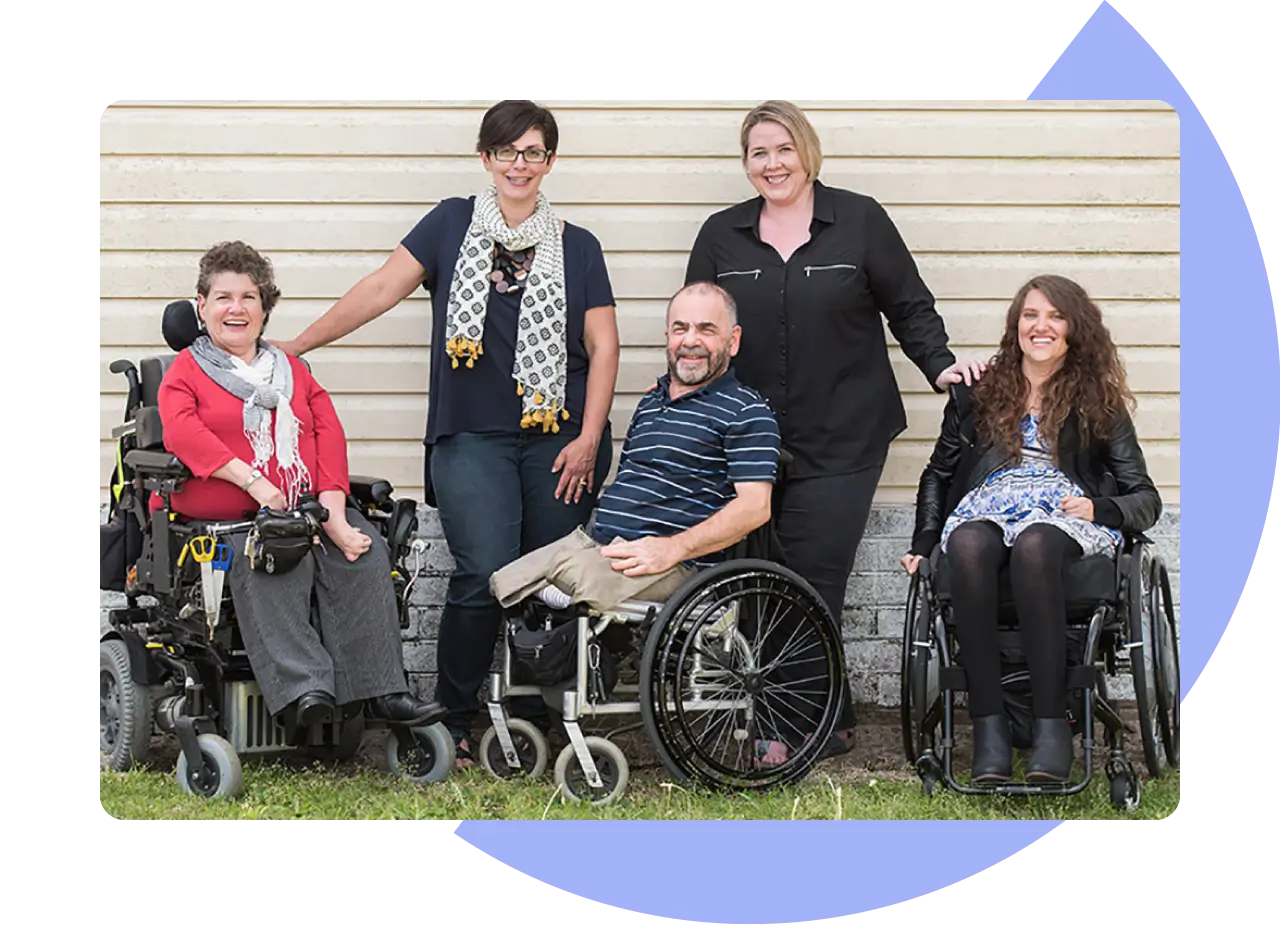 Four women and one man smiling at the camera. Two woman are standing, the man and other two women are in wheelchairs.