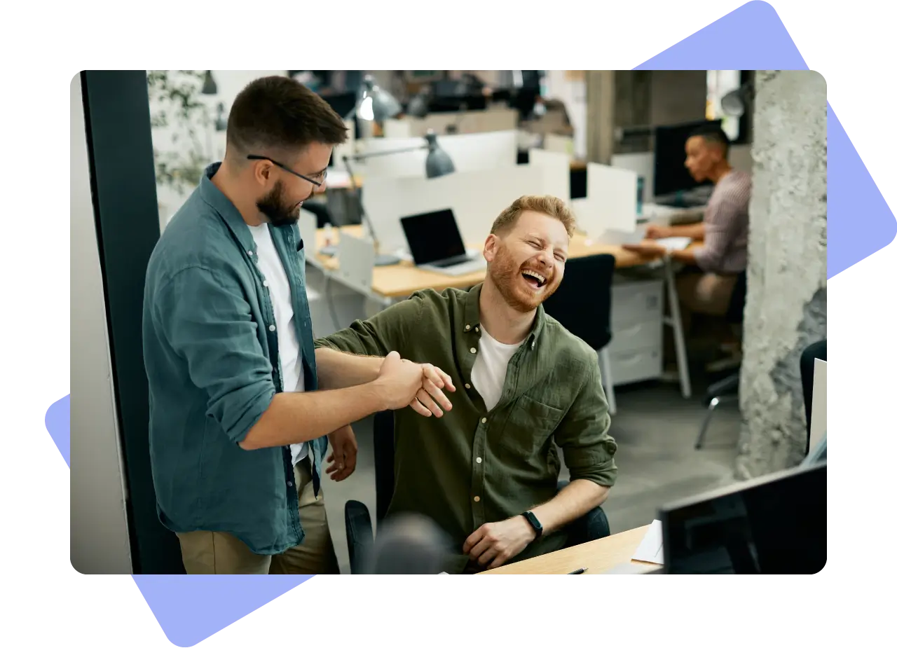 Two men laughing while greeting each other in an office.